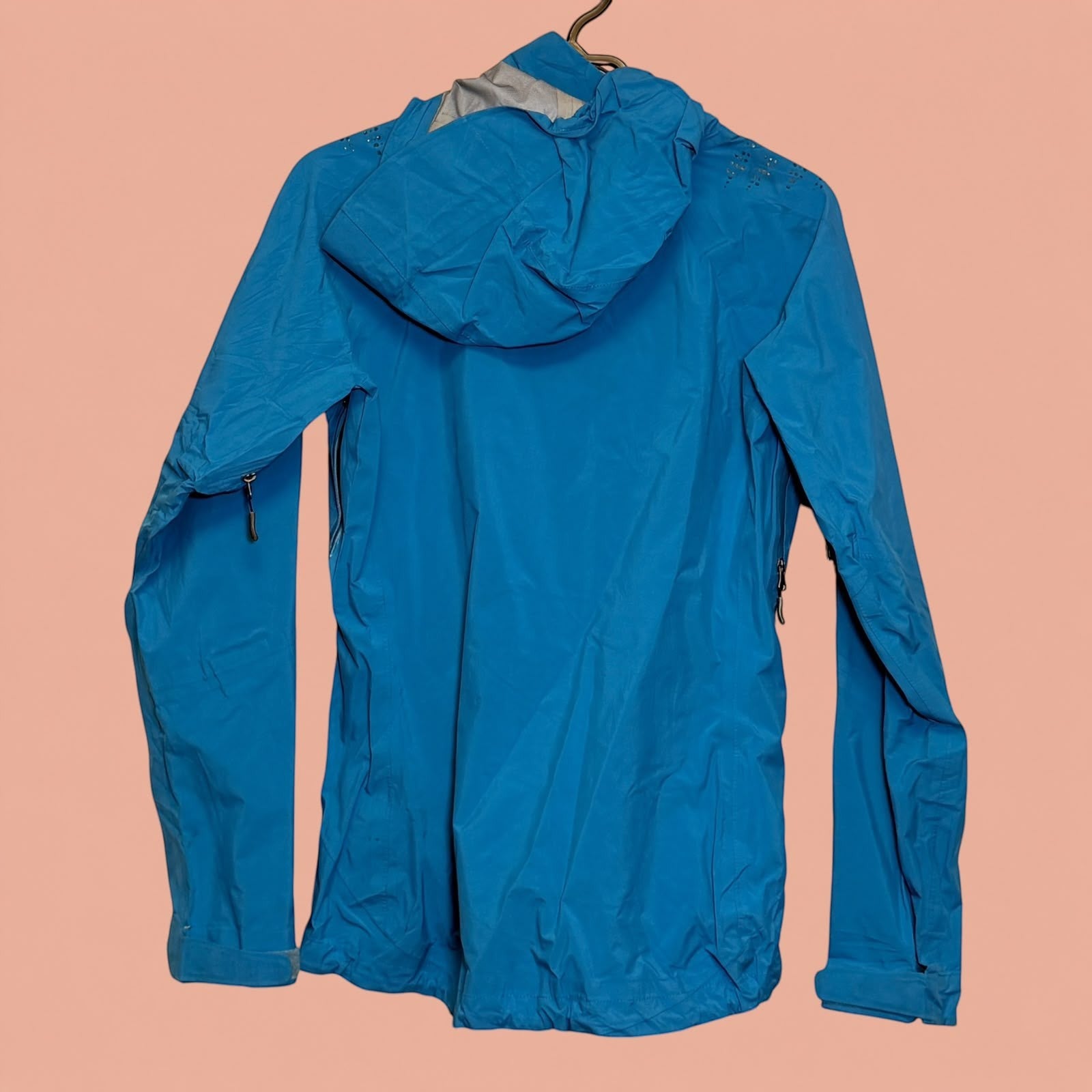 Chaqueta impermeable azul de Tuclosetrenovado.cl con capucha y cremalleras laterales, vista trasera