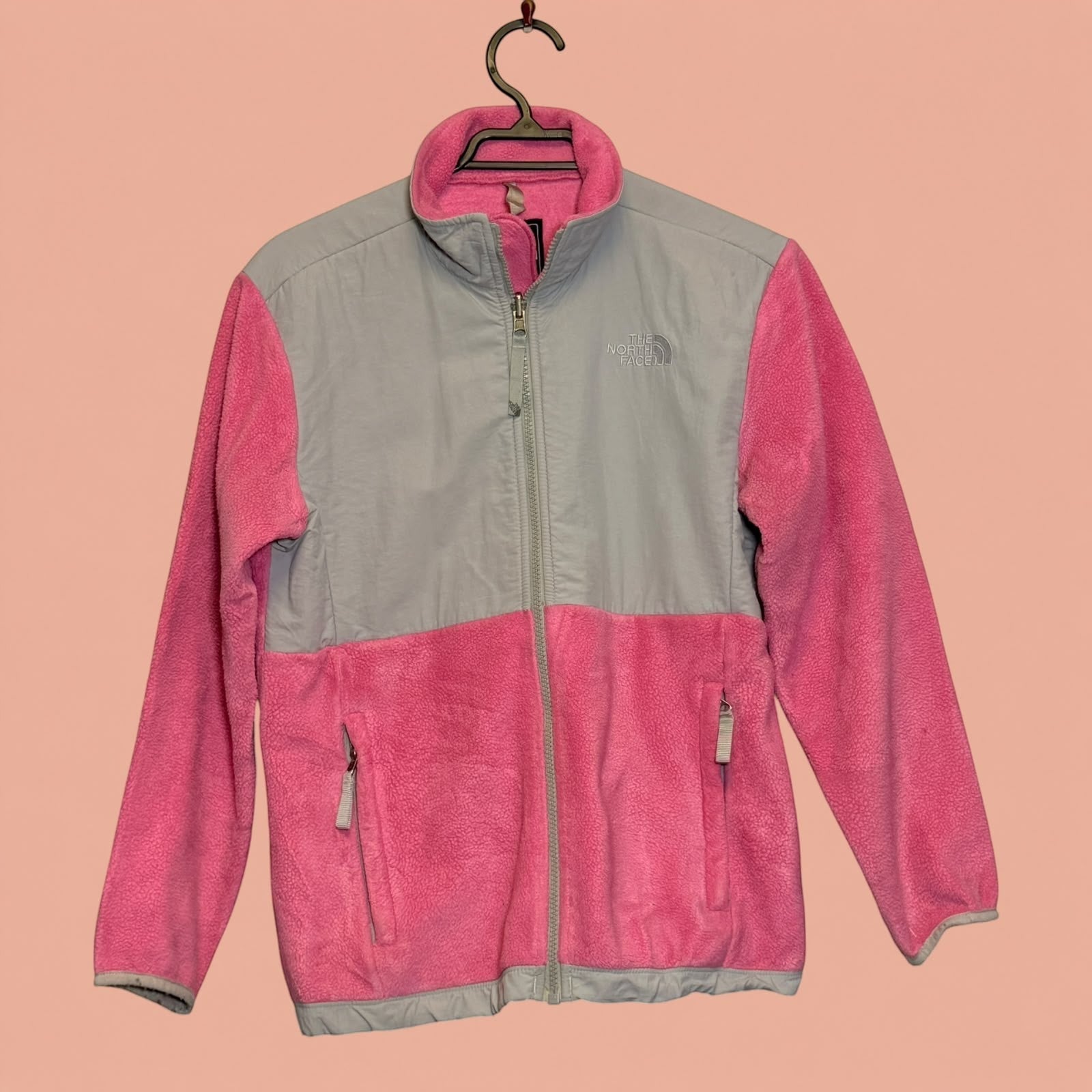 Chaqueta polar The North Face de segunda mano en color rosa y gris, con cierre frontal y bolsillos laterales.